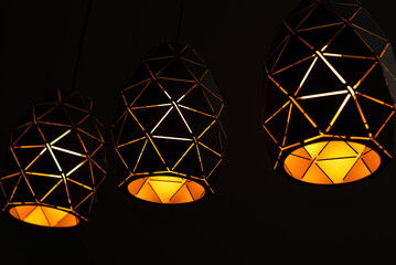 Black lamps with a geometric pattern, three lamps on a black background, burning with warm light, with a graphic pattern