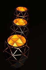 Black lamps with a geometric pattern, three lamps on a black background, burning with warm light, with a graphic pattern