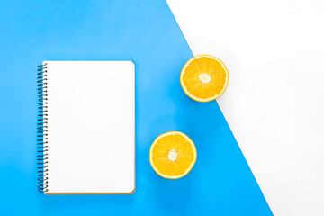 Blank notepad and orange on blue background, flat lay.