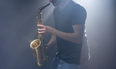 A European man plays the saxophone in the dark.