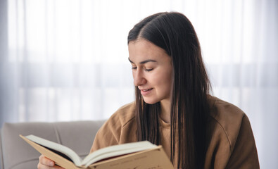 A young woman is reading a book while sitting by the window.