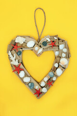 Driftwood and seashell heart shaped wreath. Symbol of romantic love and romance and natural weathered holiday travel frame. On yellow background.