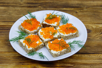 Canapes with red caviar on wooden table