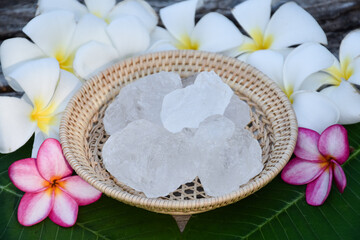 Soft focus of purple plumeria flower and white alum cube on wicker basket, spa and skincare concept.