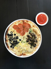 Portrait of a mixed italian pizza with hot chili dipping sauce on a black background