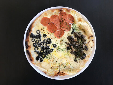 Portrait Of A Mixed Italian Pizza With Hot Chili Dipping Sauce On A Black Background