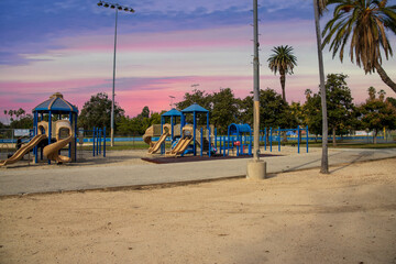 a playground with a blue and brown jungle gym and a baseball field with lush green palm trees and...