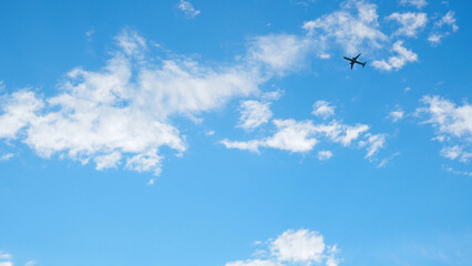 The passenger plane is flying far away in the blue sky and white clouds. Airplane in the air. International passenger air transportation. Wallpaper or background