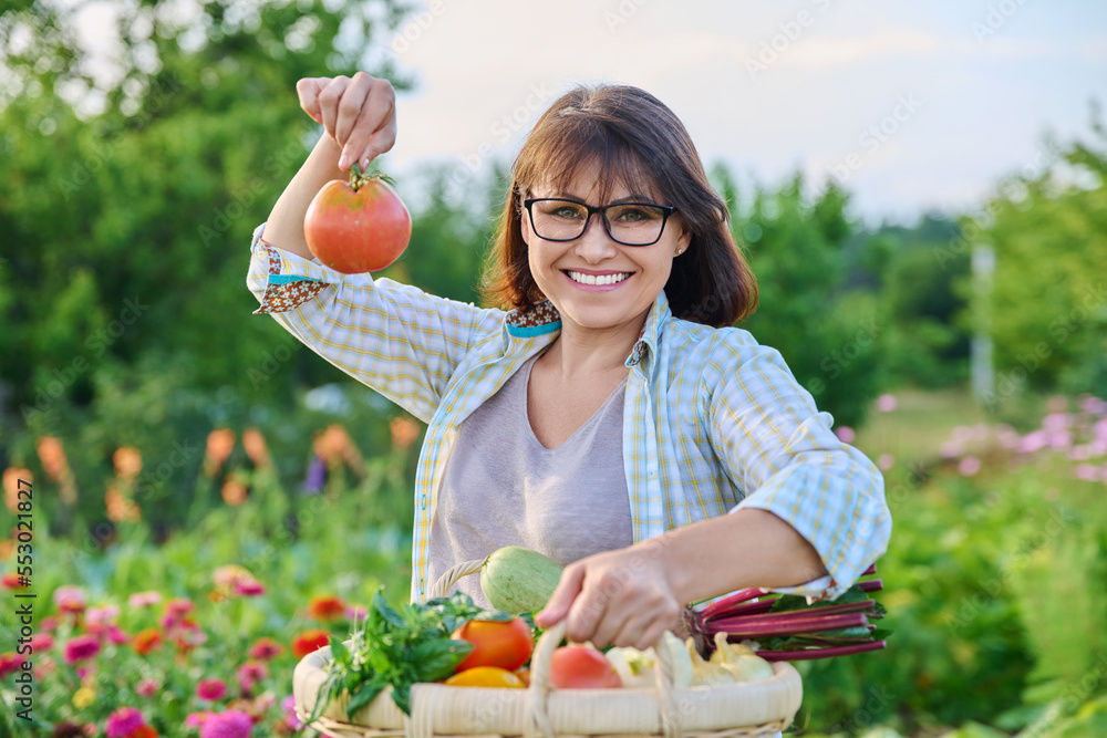 Wall mural portrait of happy farmer woman with basket of vegetables holding tomato