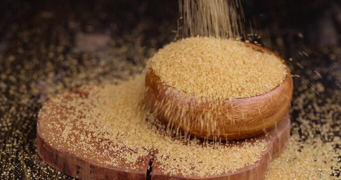 Pour natural brown cane sugar into a wooden bowl, brown sugar is poured on the table and into a wooden bowl