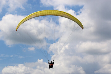 Yellow tandem Paraglider flying in a cloudy sky	