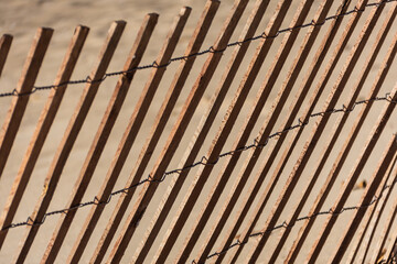 A fence in a sand dune with many diagonal lines and sunlight casting shadows.