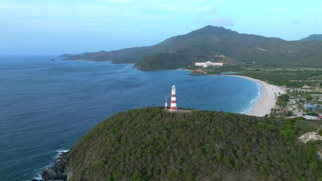 Aerial view of lighthouse on a cliff of the seashore. High mountains and Hesperia Isla Margarita resort in the background. Punta Zaragoza, Venezuela