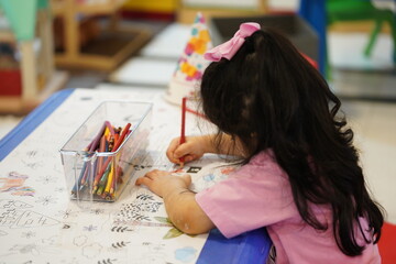 A child sits and colours a giant colouring paper pattern. Child holds a pencil in his hand. A set of coloured pencils on a box. Drawing activities for kids preschool. Learning drawing for kids