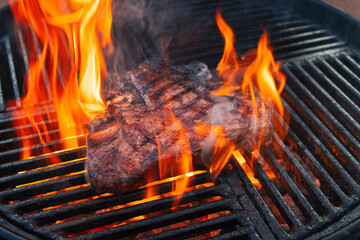 Barbecue dry aged wagyu porterhouse beef steak grilled as close-up on a charcoal grill with fire...