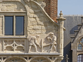 Bas relief sculpture of dockworkers holding an anchor on a medieval guild house in the port of Ghent