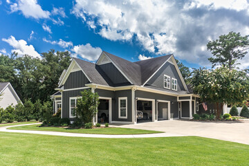 The side view of a large gray craftsman new construction house with a landscaped yard a three car...
