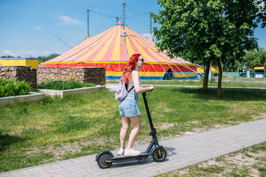 Young bright woman smiles and rides electric scooter in the summer in the city