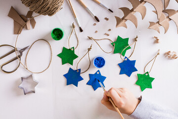 A girl paints a gouache star out of cardboard for DIY handmade Christmas decorations. Top view.