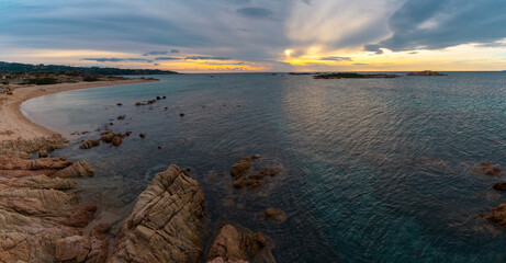 panorama view of a golden sand beach at sunset with calm ocean water and red granite rocks
