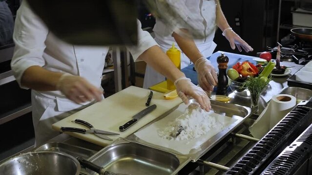Close-up of the chef sprinkling salt on raw fish before baking in the oven. The process of cooking Dorado fish in a large amount of salt in a professional kitchen.