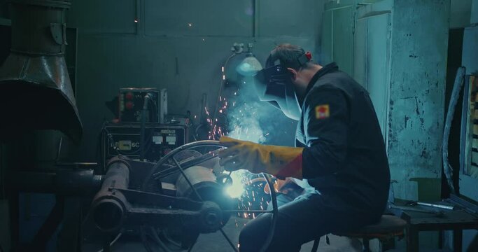 Professional welder is sitting in the workshop at the factory. Work by electric arc welding.