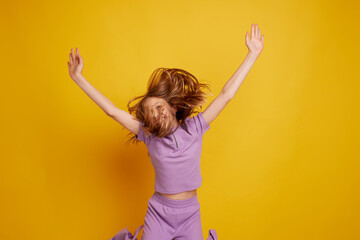 A beautiful young girl is dancing, laughing and having fun on a clean yellow background