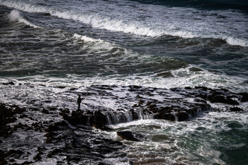 Silhouette of a man fishing in the Atlantic Ocean during high tide.