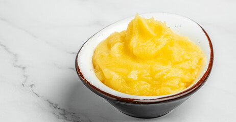 Pure OR Desi Ghee also known as clarified liquid butter in a bowl with wooden spoon on a light background. Long banner format