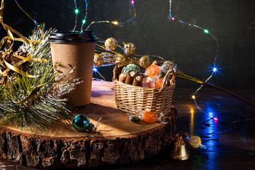 Coffee glass and Christmas toys. Festive coffee and sweets. Cardboard glass for drinks on a wooden stand.