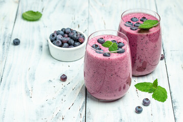 Bilberry smoothie yogurt, fresh blueberries in glass with mint leaf and raw beeries on white background. Restaurant menu, dieting, cookbook recipe top view