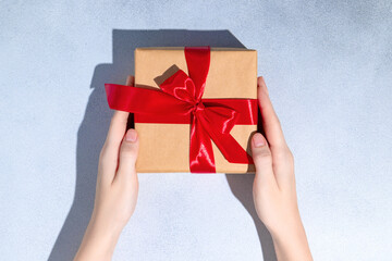 Female hands hold gift box with red ribbon on grey background. Copy space for design.
