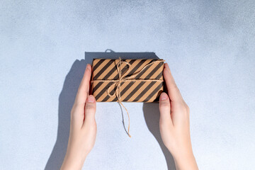 Female hands hold gift box or present wrapped in craft paper. Holiday present. Copy space. Mockup.
