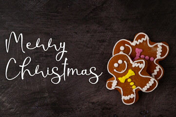 Two gingerbread men with colorful icing placed in the lower corner of the image on a black metallic background with label "Merry christmas". Top view.