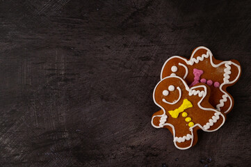 Two gingerbread men with colorful icing placed in the lower corner of the image on a black metallic background. Copy space. Top view.