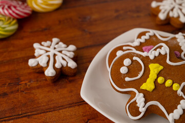 Obraz na płótnie Canvas Two gingerbread men with colorful icing on a white dessert plate on a wooden table with gingerbread and caramels in the background.