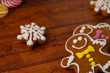 Close-up of gingerbread men with colorful icing on a wooden background with gingerbread and caramels in the background.