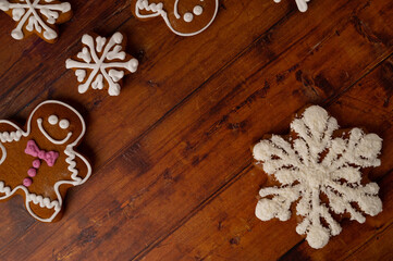 Star-shaped gingerbread with coconut shards frosting on a brown wooden table background, different shapes of gingerbread can be seen in the background. Top view.