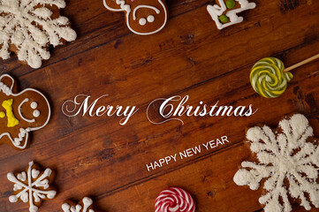 Christmas greeting concept - a brown wooden table background surrounded by various shaped gingerbreads with glaze and caramels with copy space in a middle. Top view.