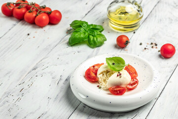 Creamy Italian Burrata Cheese with basil, olive oil and cherry tomatoes on white plate on light wooden background. banner, menu, recipe place for text, top view