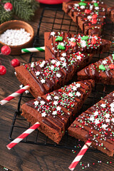 Chocolate brownies Christmas tree with chocolate icing and festive sprinkles on wooden table. Christmas food ideas sweet homemade Christmas holidays pastry concept. Holiday cooking concept. Top view.