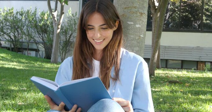 Young smiling woman reading a book in a park under a tree 