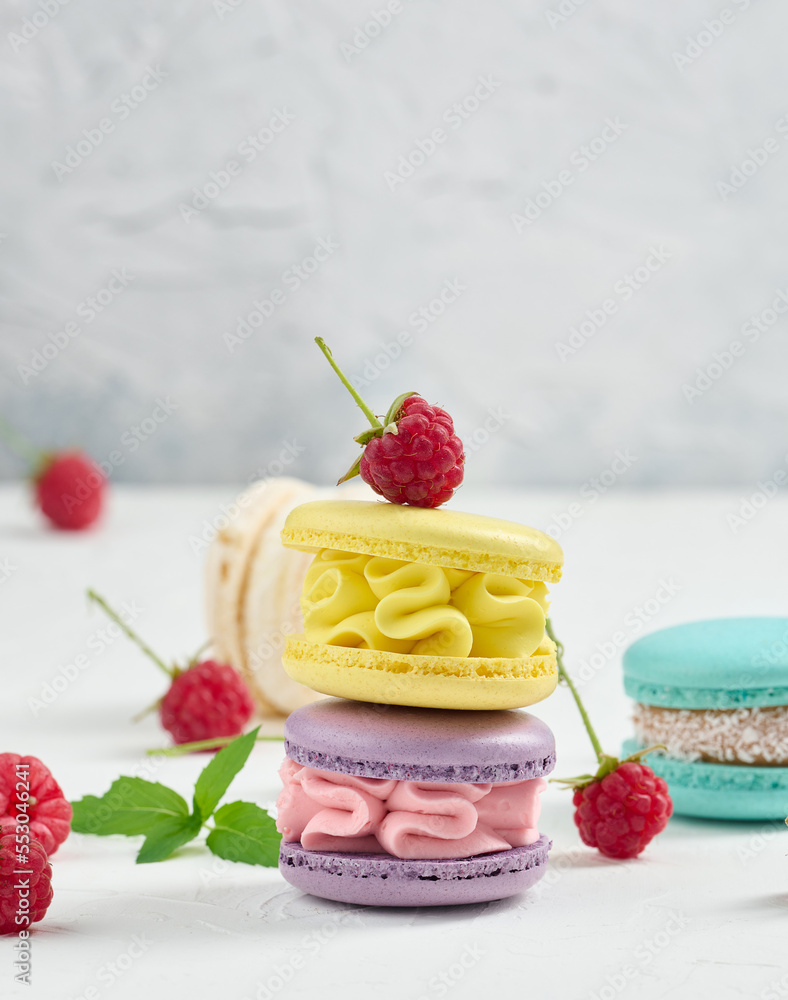 Poster stack of multicolored macaroons and red raspberries on a white background.