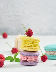 Stack of multicolored macaroons and red raspberries on a white background.