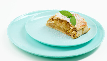Slice of apple strudel on a round plate, white background