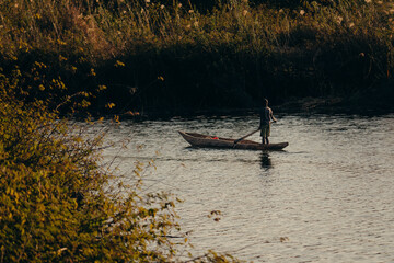 Idyllische Abendszene am Okavango -Ein Junge stakt im Dämmerungslicht mit Einbaum Boot über den...