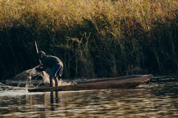 Idyllische Abendszene am Okavango - Ein Junge fischt mit Netz von seinem Einbaum Boot aus im...