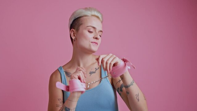 Portrait view of the tattooed blonde woman wearing bdsm handcuffs smiling playfully