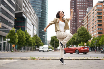 Portrait of asian happy girl jumping and dancing in city centre, posing on streets, express joy and...