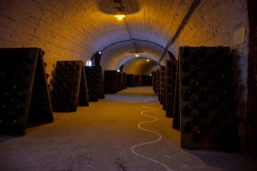 Walking in deep and long undergrounds caves with dusty bottles on racks, making champagne sparkling wine from chardonnay and pinor noir grapes in Epernay, Champagne, France